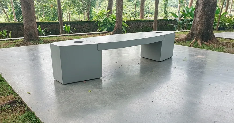 Banca de concreto blanca con espaldar de Vivero Harmony, instalada en un patio de baldosas con un jardín de fondo.