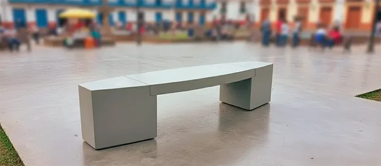 Los 3 Criterios Esenciales al Elegir Bancas de Concreto para Exterior 1 Banca de concreto moderna sin espaldar, instalada en una plaza pública de un pueblo colombiano, con personas y edificios coloniales al fondo.